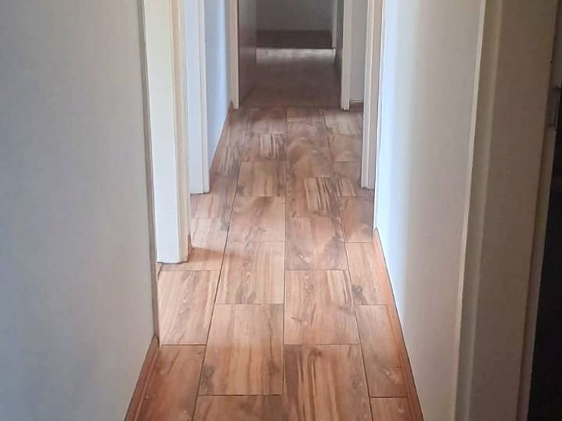A narrow interior hallway featuring wood-look tile flooring and a central pendant light fixture, providing access to multiple rooms.