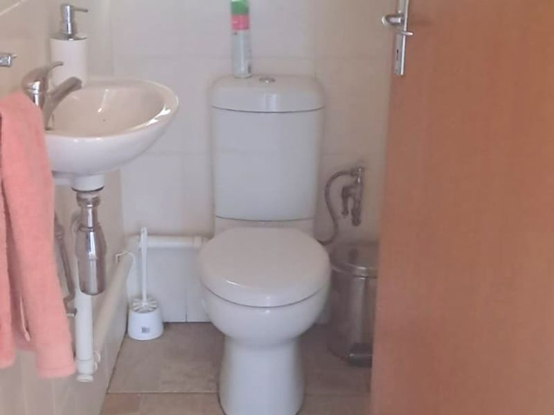 A compact office restroom featuring a wall-mounted basin, a standard toilet, and tiled flooring.