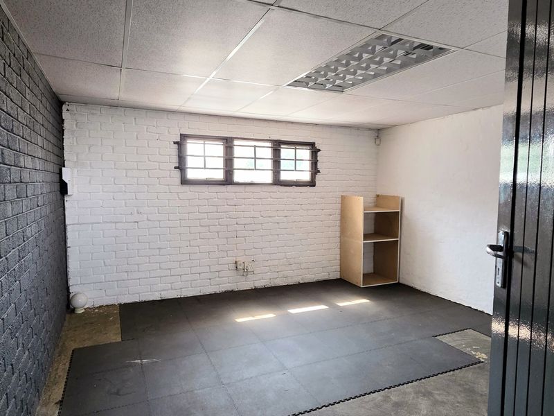 A functional utility space featuring exposed brick walls, a suspended ceiling with recessed lighting, and security bars on the window.