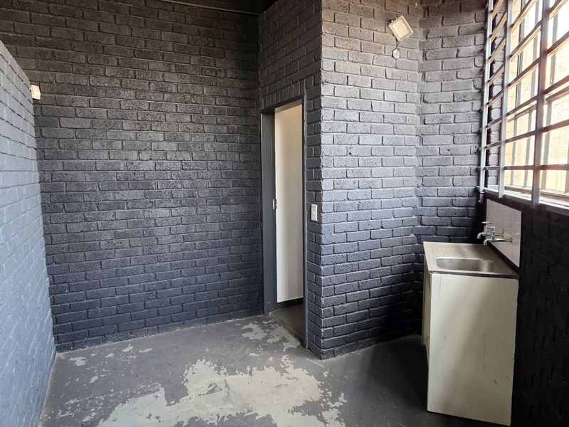 A functional industrial utility space featuring painted brick walls, concrete flooring, and a built-in utility sink with security bars on the windows.
