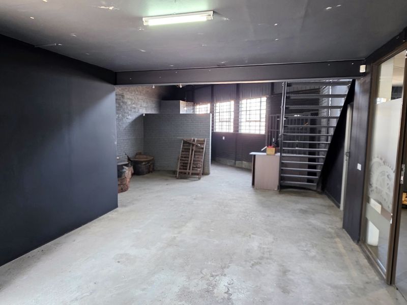 Spacious industrial open-plan area featuring exposed steel beams, concrete flooring, and a metal staircase, offering a versatile layout for various commercial uses.