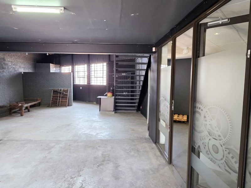 Spacious industrial open-plan area featuring exposed brick walls, a metal staircase, and a modern glass partition with decorative frosted detailing.