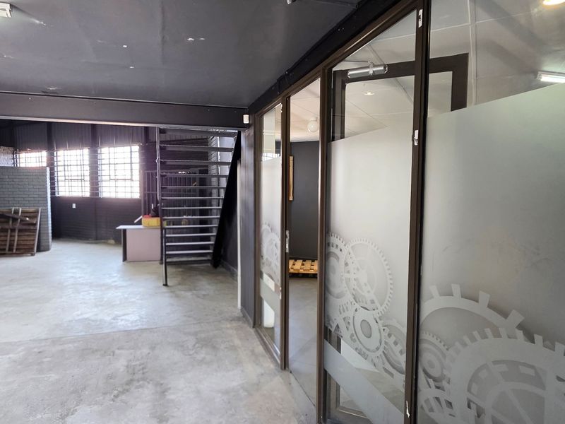 Spacious industrial open-plan area featuring exposed brick walls, concrete flooring, a steel staircase, and modern glass partitioned office spaces.