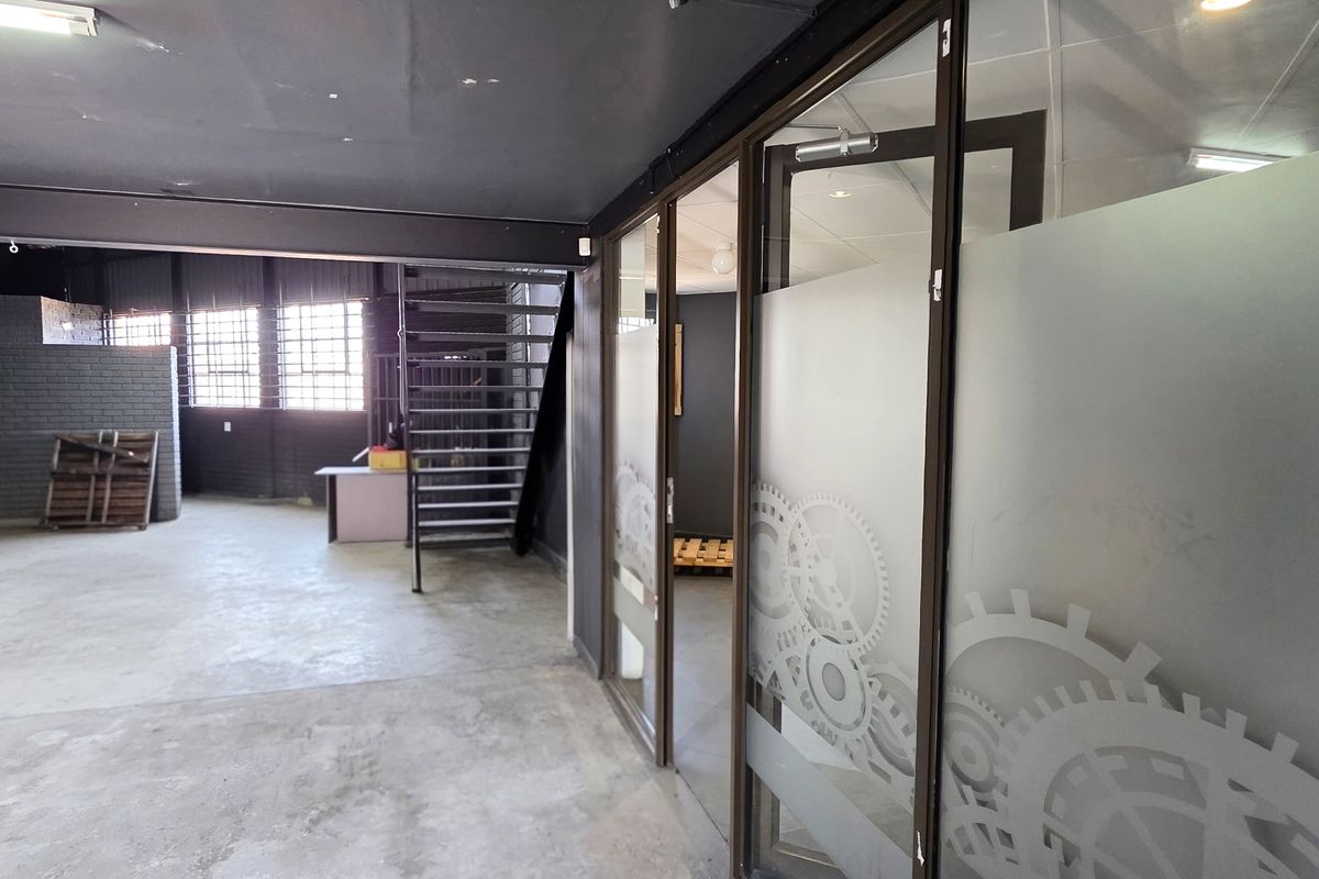 Spacious industrial open-plan area featuring exposed brick walls, concrete flooring, a steel staircase, and modern glass partitioned office spaces.