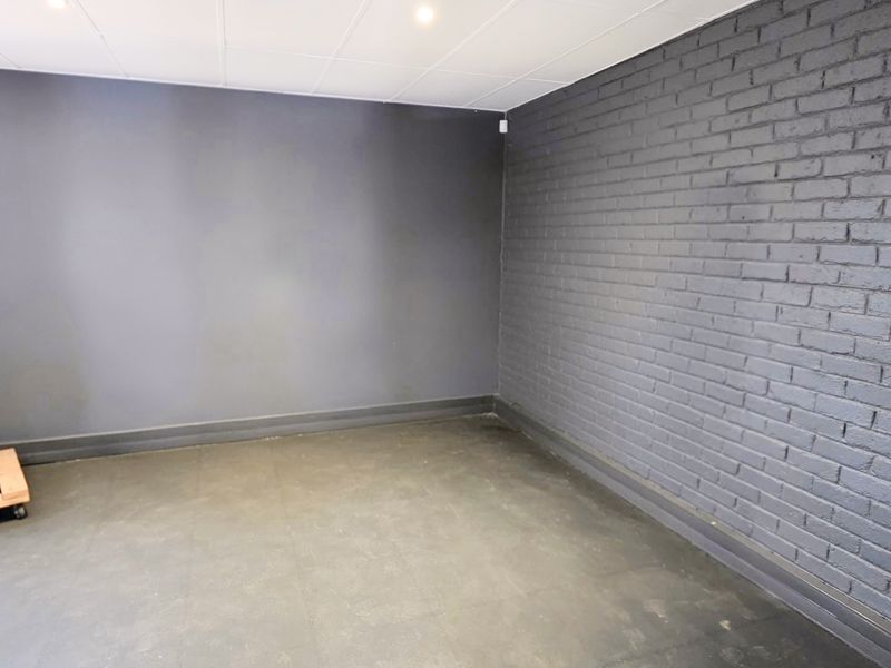 A clean, empty utility space featuring dark painted brick walls, recessed ceiling lighting, and durable flooring, suitable for various industrial or storage purposes.