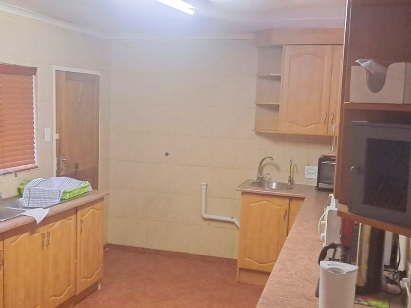 A functional office kitchen area featuring wooden cabinetry, dual stainless steel sinks, and tiled flooring, providing essential utility space for staff.