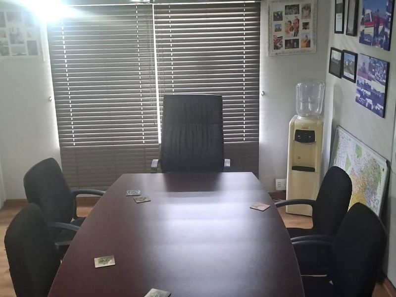 A functional office meeting room featuring wood-look flooring, horizontal window blinds, and built-in storage cupboards.