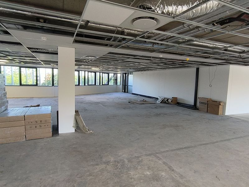 An open-plan office space currently under renovation, featuring an exposed ceiling grid, large windows, and unfinished flooring ready for fit-out.