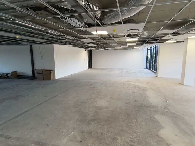 An expansive, open-plan office space currently under renovation, featuring exposed ceiling infrastructure, concrete flooring, and large windows providing ample natural light.