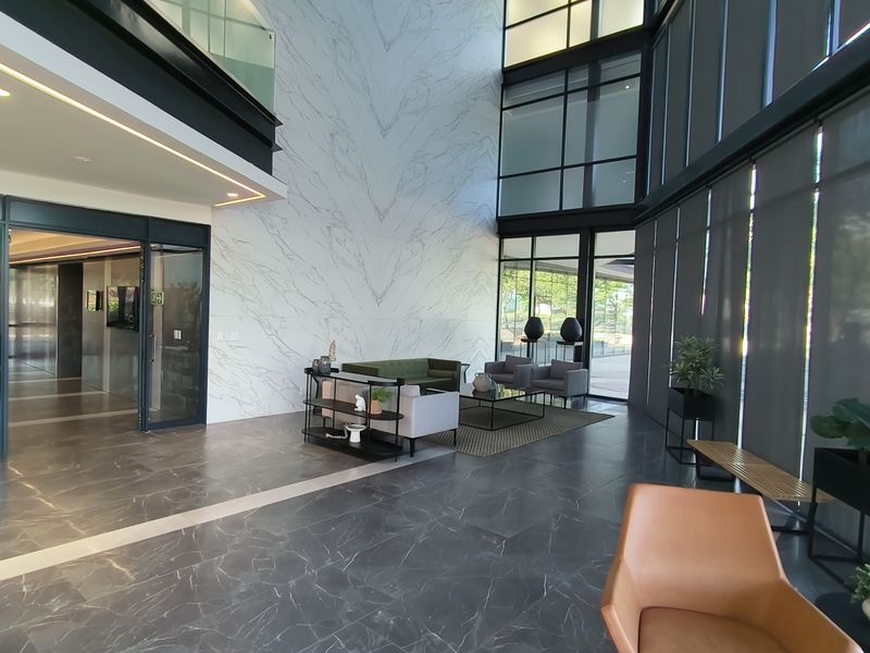 Spacious double-volume office lobby featuring high-end marble-look wall finishes, extensive floor-to-ceiling glass windows, and premium stone flooring.