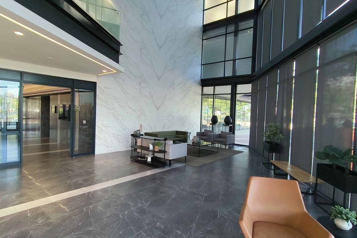 Spacious double-volume office lobby featuring high-end marble-look wall finishes, extensive floor-to-ceiling glass windows, and premium stone flooring.
