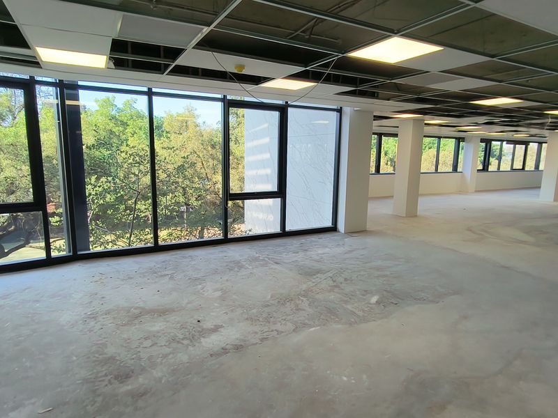 A large, open-plan office space currently under renovation, featuring expansive windows with natural light and an unfinished ceiling and floor.