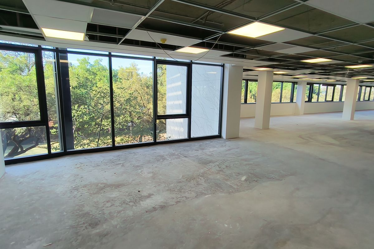 A large, open-plan office space currently under renovation, featuring expansive windows with natural light and an unfinished ceiling and floor.