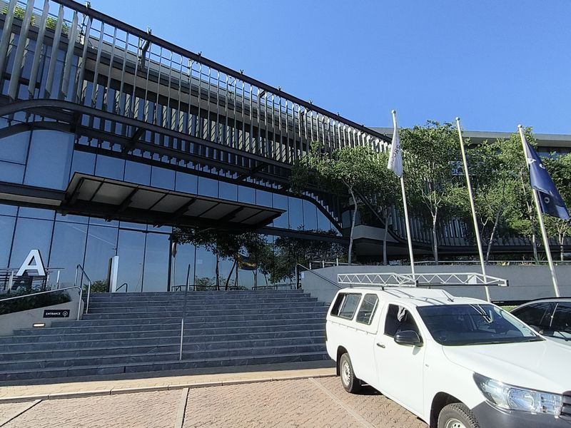Modern office building facade featuring a glass curtain wall, prominent stone entrance staircase, and architectural metal sun louvers.