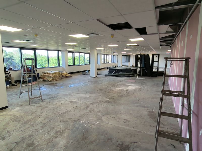 Open plan office space currently undergoing renovations with exposed drywall, missing ceiling tiles, and unfinished flooring.