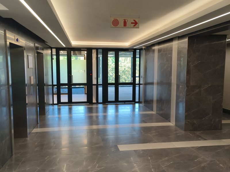 Modern office building lobby featuring polished marble wall and floor finishes, recessed architectural lighting, and dual elevator access.