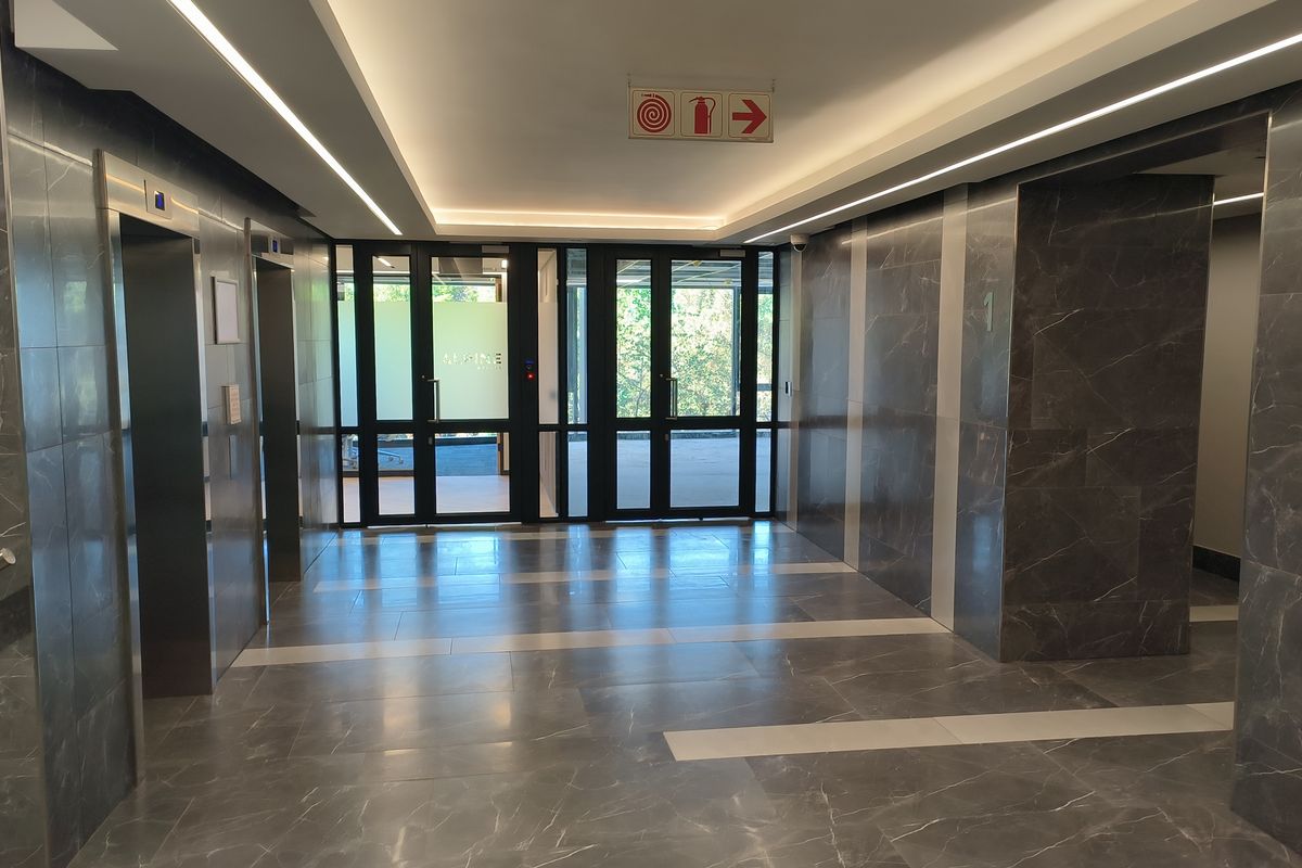 Modern office building lobby featuring polished marble wall and floor finishes, recessed architectural lighting, and dual elevator access.