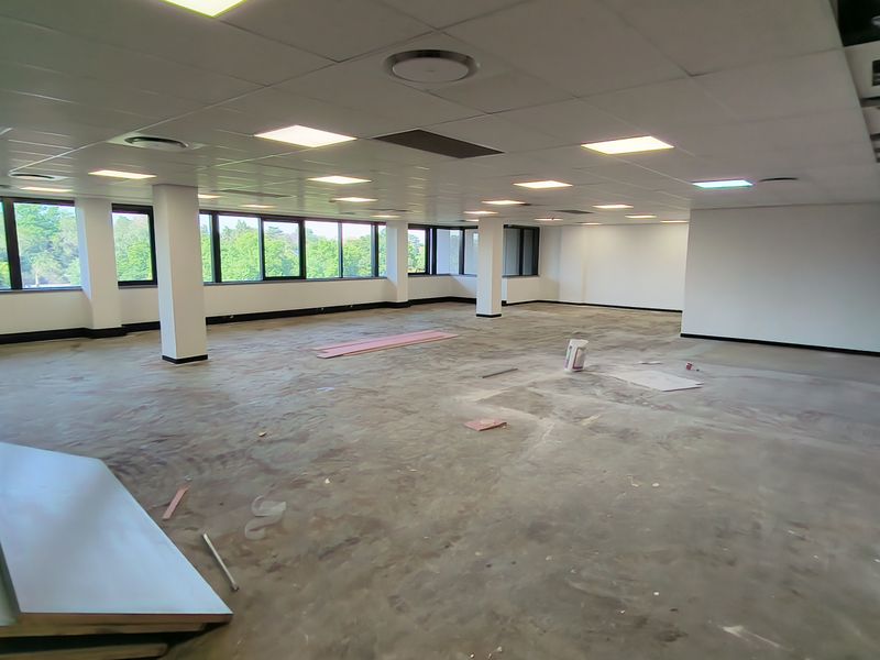 A large, open-plan office space featuring a suspended ceiling, recessed lighting, and expansive windows, currently in an unfinished state.
