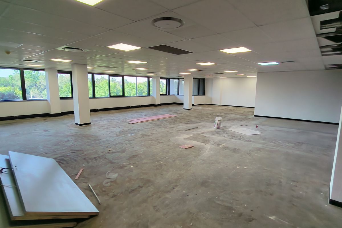 A large, open-plan office space featuring a suspended ceiling, recessed lighting, and expansive windows, currently in an unfinished state.