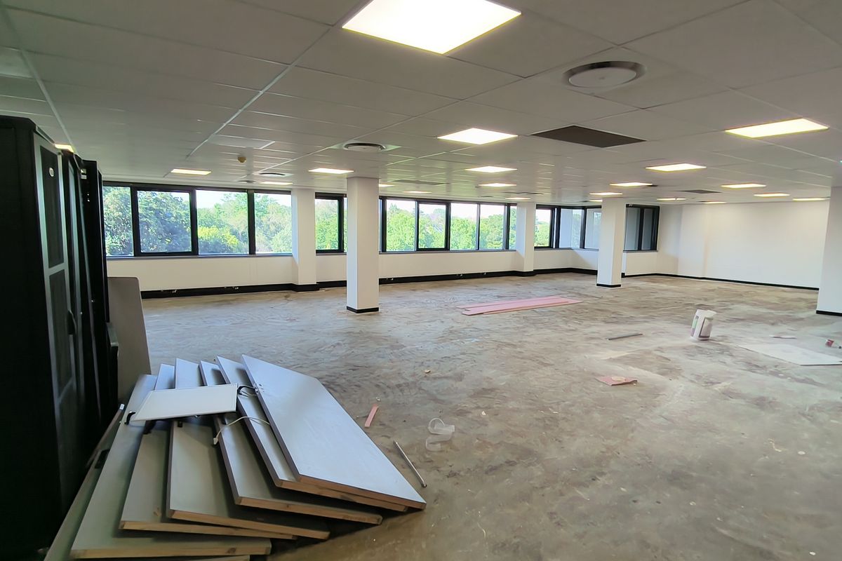 Spacious open-plan office area featuring a suspended ceiling with recessed lighting, large windows providing natural light, and an unfinished floor ready for customization.