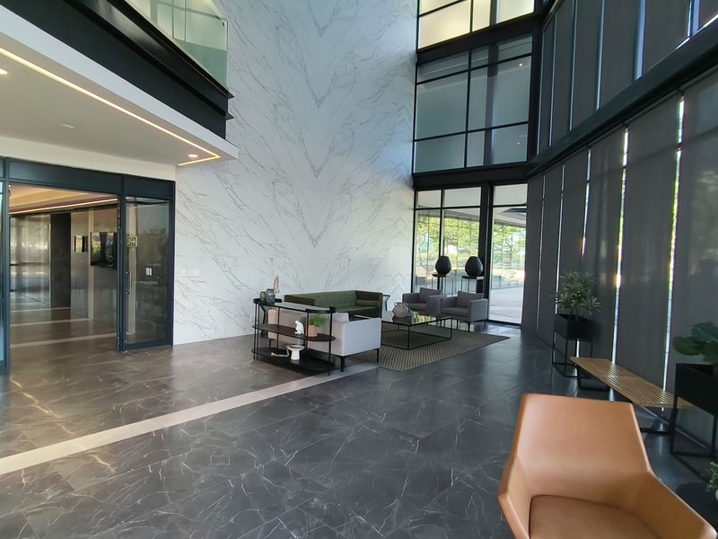A spacious, modern office building lobby featuring high ceilings, marble-look wall finishes, and extensive floor-to-ceiling glass windows providing ample natural light.