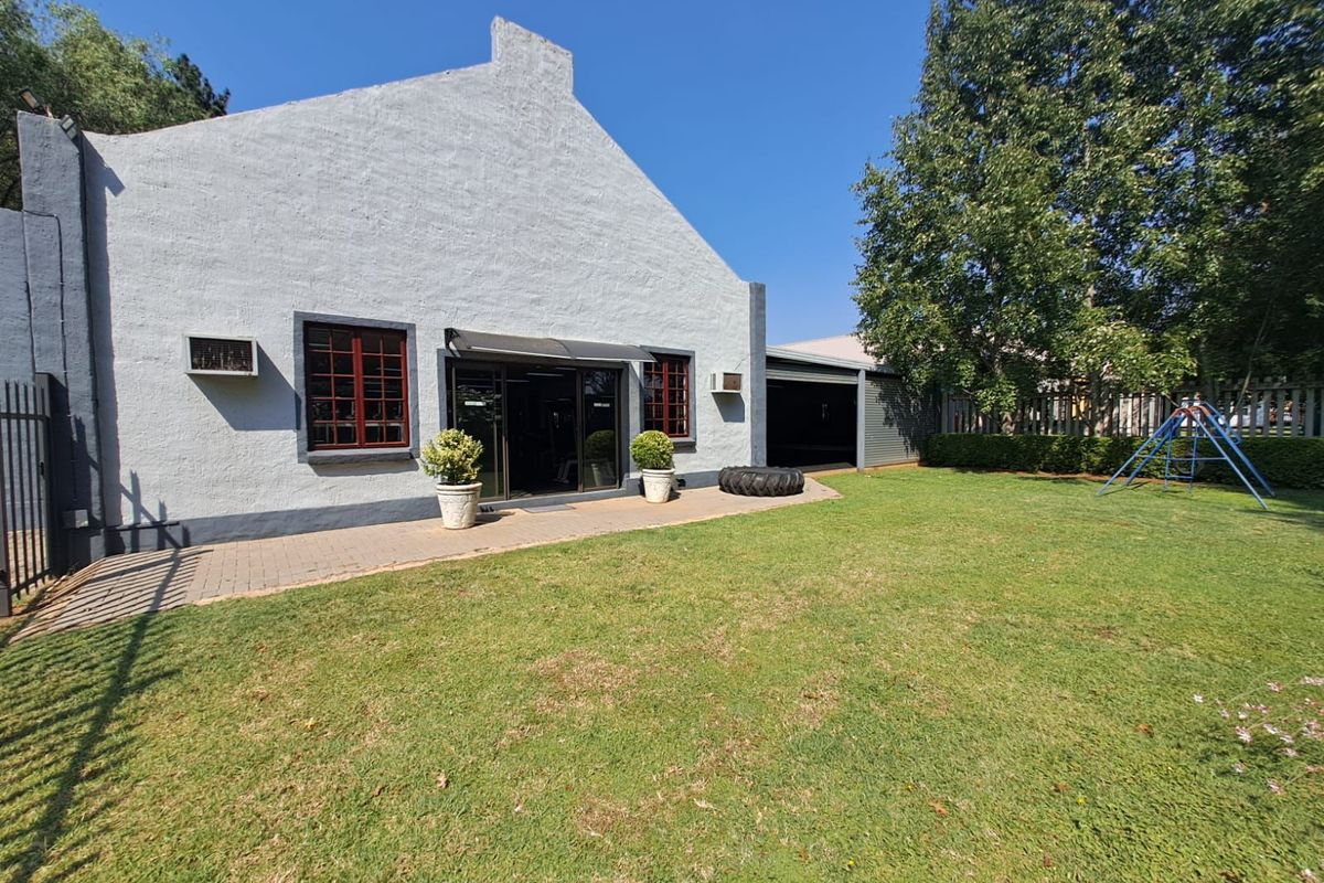 Rear view of the commercial property featuring a paved patio area, landscaped lawn, and access to a garage space.