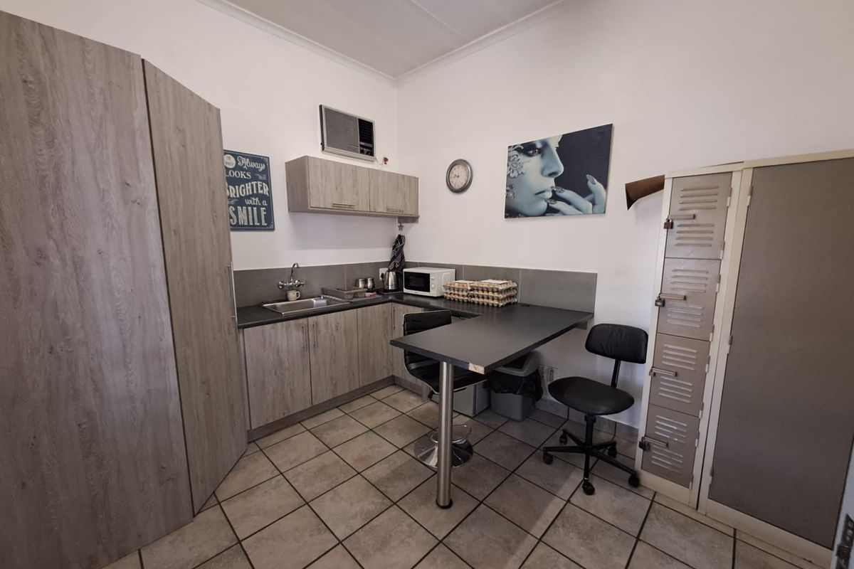 Compact kitchenette featuring wood-look cabinetry, a stainless steel sink, tiled flooring, and a built-in breakfast bar area.