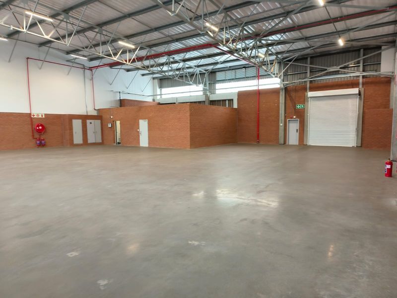 Spacious industrial warehouse unit featuring high ceilings with exposed steel trusses, polished concrete flooring, and a large roller shutter door for easy access.