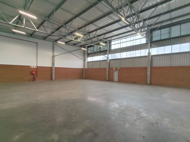 Spacious industrial warehouse unit featuring high ceilings with exposed steel trusses, polished concrete flooring, and ample natural light through high-level windows.