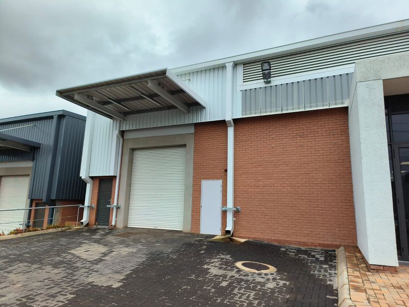 Industrial warehouse unit featuring a roller shutter door, loading canopy, and brick facade with paved exterior access.