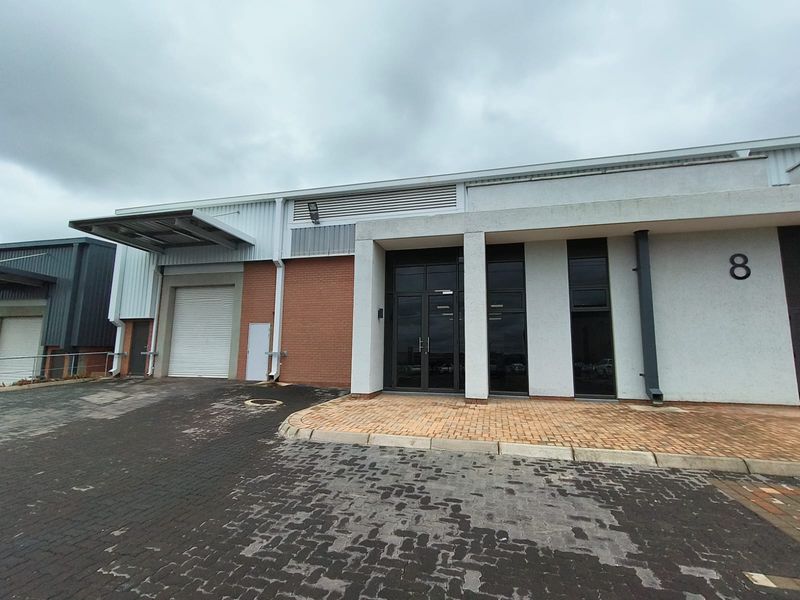 Front elevation of an industrial unit featuring a roller shutter door, glass entrance, and paved driveway access.