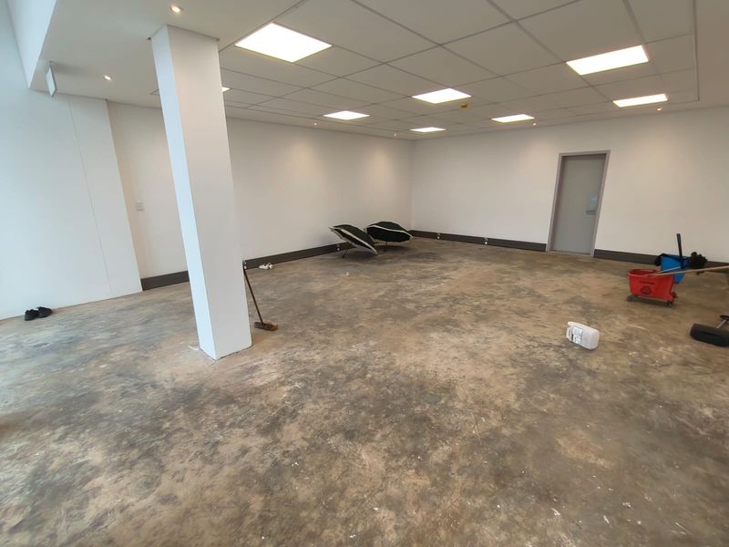 An open-plan industrial space featuring a suspended ceiling with recessed lighting, a structural column, and worn concrete flooring.
