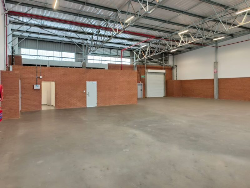 Spacious industrial warehouse unit featuring high ceilings with exposed steel trusses, concrete flooring, roller shutter access, and functional face brick walling.