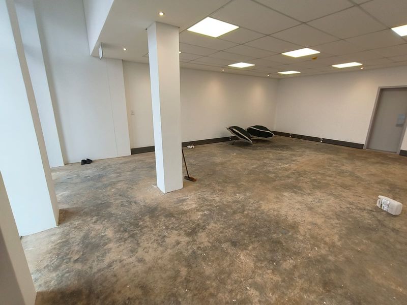 An open-plan industrial space featuring a suspended ceiling with recessed lighting, a structural column, and unfinished concrete flooring.
