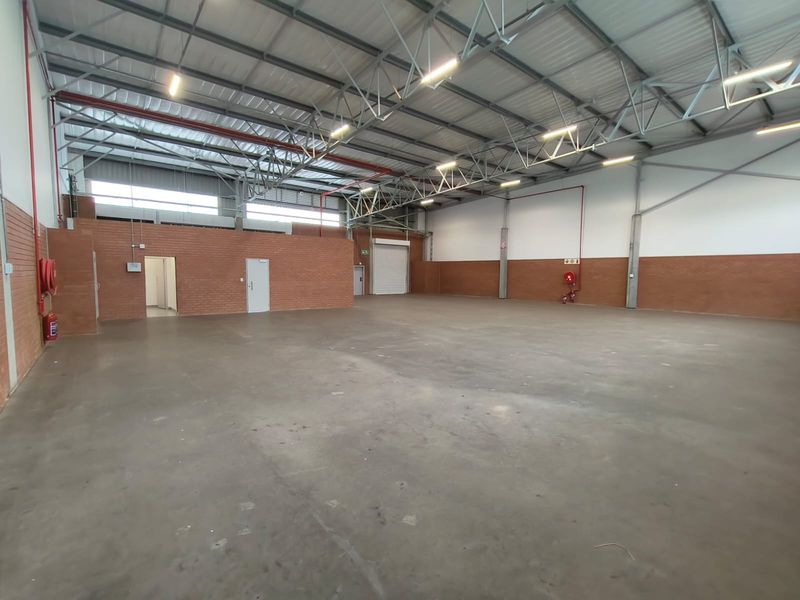 Spacious industrial warehouse unit featuring high ceilings with exposed steel trusses, concrete flooring, and a roller shutter door for efficient access.