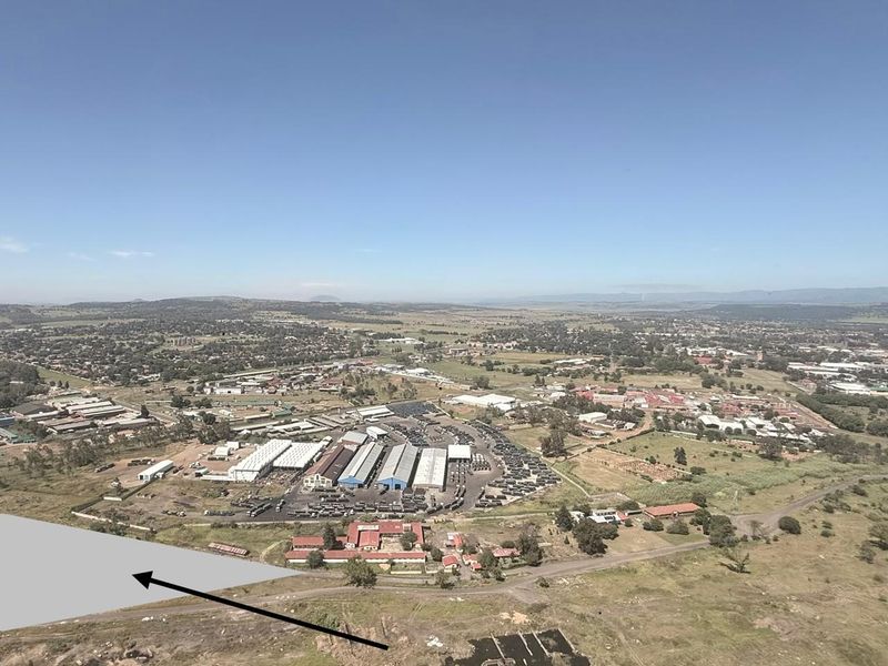 Aerial view of an industrial facility complex situated within a rural landscape, featuring multiple warehouse structures and extensive parking areas.