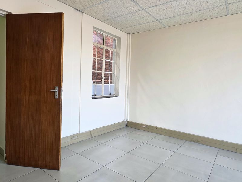 A vacant office space featuring tiled flooring, a suspended ceiling, and natural light through multi-pane windows, suitable for a professional workspace.