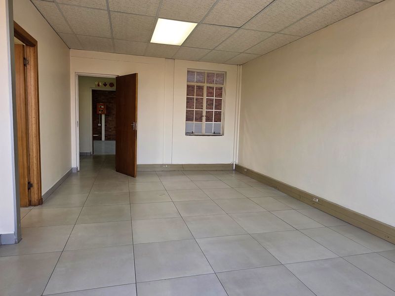 A vacant, well-lit office space featuring neutral tiled flooring, a suspended ceiling with recessed lighting, and timber door frames.