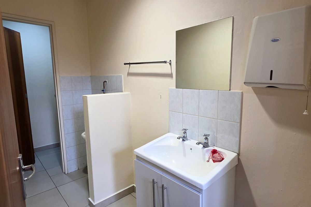 A functional bathroom featuring a vanity basin, wall-mounted mirror, and tiled splashback, with a separate partitioned toilet area.