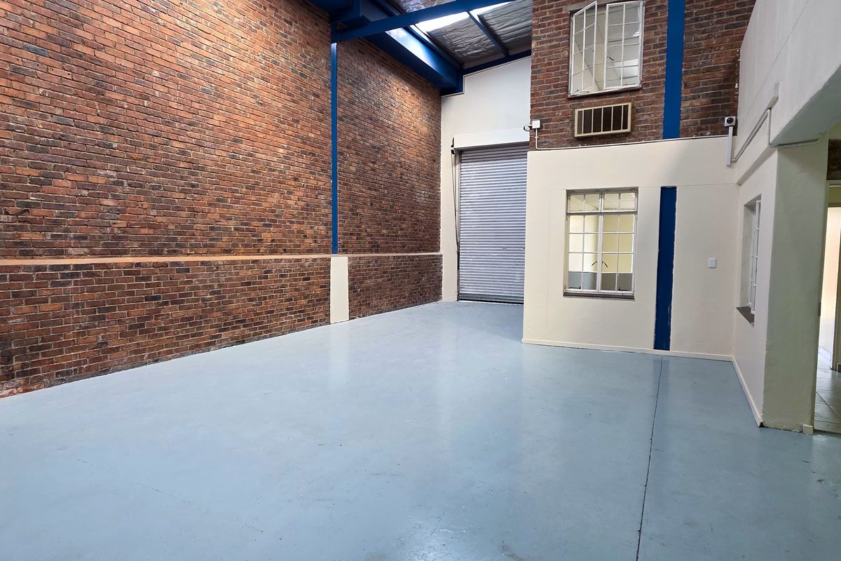 Spacious industrial utility area featuring exposed brick walls, high ceilings with skylights, a roller shutter door, and durable painted concrete flooring.