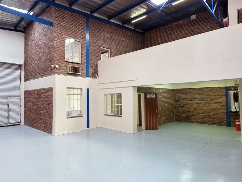 Spacious industrial warehouse unit featuring high ceilings, exposed brickwork, a large roller shutter door, and a functional mezzanine level for additional storage or office space.