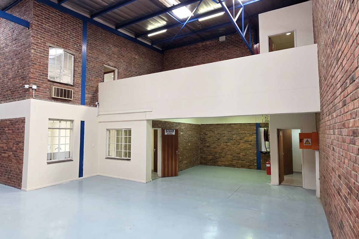 Spacious industrial warehouse unit featuring exposed brick walls, high ceilings with steel trusses, a mezzanine level, and a durable epoxy-coated floor.