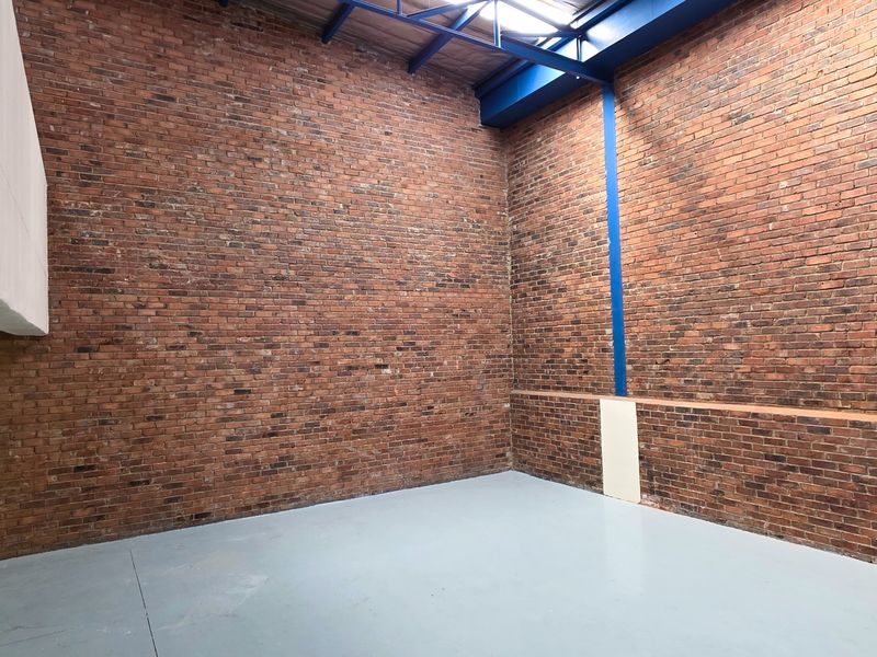 Spacious industrial utility area featuring high ceilings, exposed brick walls, and durable painted concrete flooring, suitable for various commercial or storage applications.