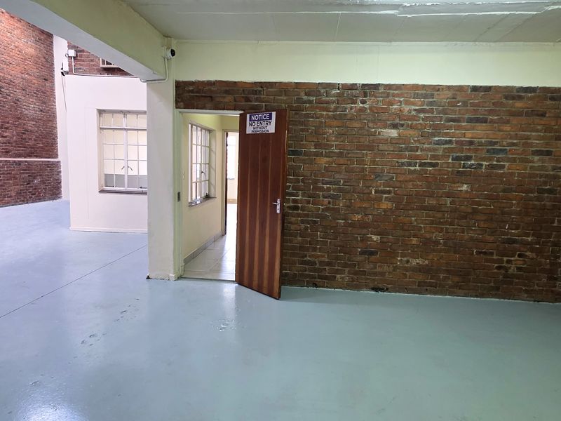 Spacious industrial open-plan area featuring exposed brick walls, painted concrete flooring, and high ceilings, offering a versatile layout for various commercial uses.