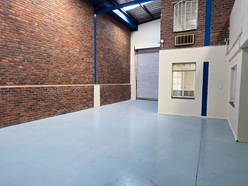 Spacious industrial utility area featuring exposed brick walls, high ceilings with skylights, a roller shutter door, and durable painted concrete flooring.