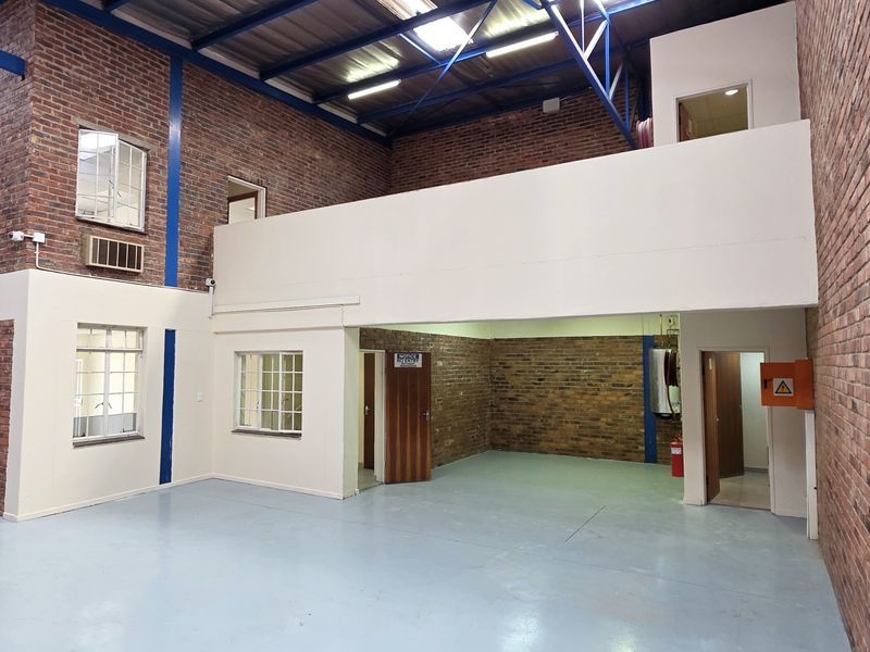 Spacious industrial warehouse unit featuring exposed brick walls, high ceilings with steel trusses, a mezzanine level, and a durable epoxy-coated floor.