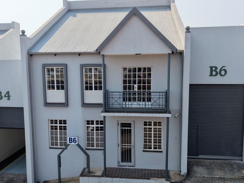 Front elevation of an industrial unit featuring a corrugated metal roof, roller shutter doors, and a balcony with metal railing.