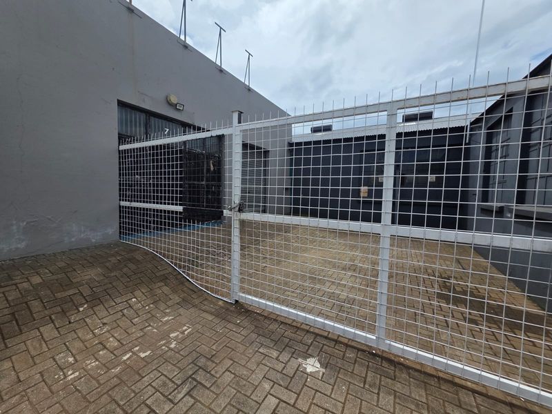 A secure, paved outdoor utility area featuring a white wire mesh gate and perimeter fencing, suitable for business storage or access.