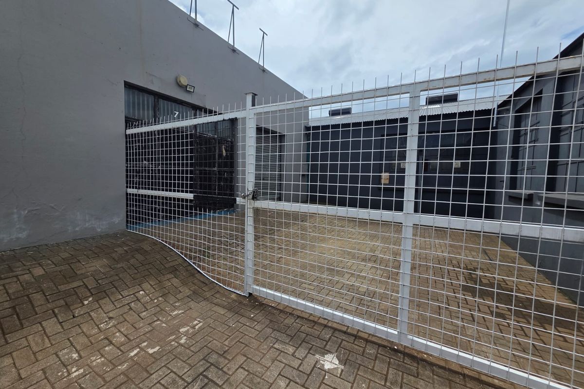 A secure, paved outdoor utility area featuring a white wire mesh gate and perimeter fencing, suitable for business storage or access.