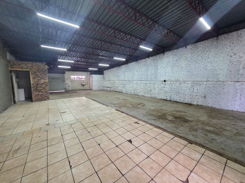Spacious industrial warehouse or commercial space featuring exposed brick walls, tiled and concrete flooring, and high-clearance ceilings with integrated lighting.